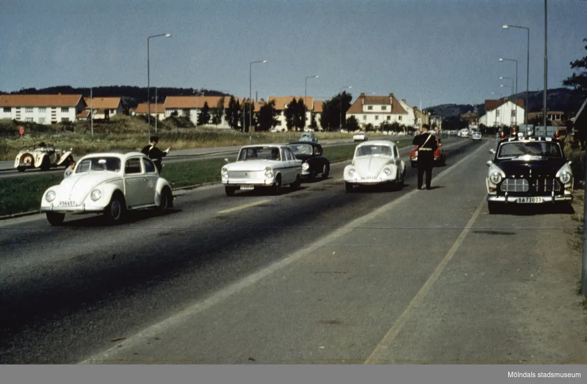 Poliskontroll på Kungsbackavägen i Mölndal, då vi fortfarande hade vänstertrafik, cirka 1965 - 1966. Högertrafik infördes september 1967. I bakgrunden ses bebyggelse i Broslätt.