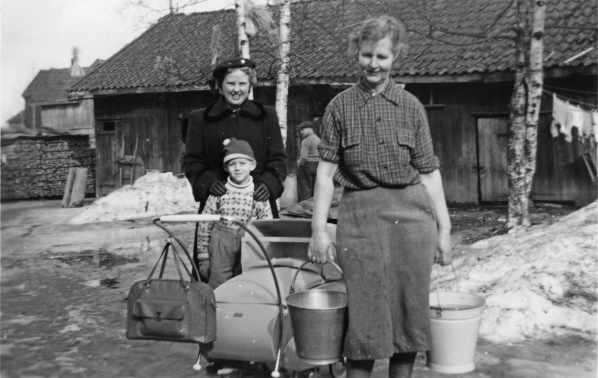To damer med barn, barnevogn, melkespann og stor veske i bakgården på Brandvoldboligen 1953.