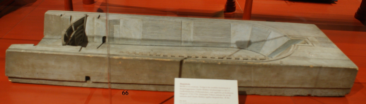 Modell av torrdocka, tillverkad i tre stycken, med delvis trappstegsformade långsidor och ett uttag längst in för fartygens stäv samt med dockport i ett stycke.
Av trä, gråmålad.