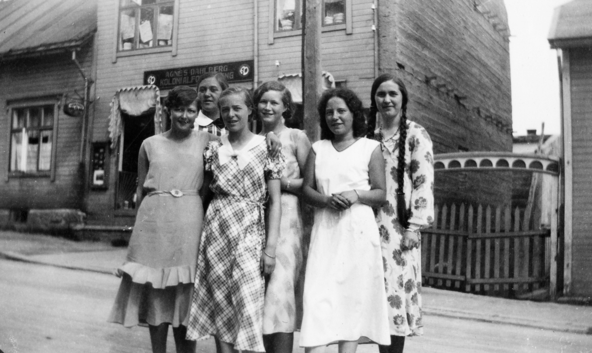 Seks unge kvinner fotografert i bygate, foran kolonialbutikken til Agnes Dahlberg.