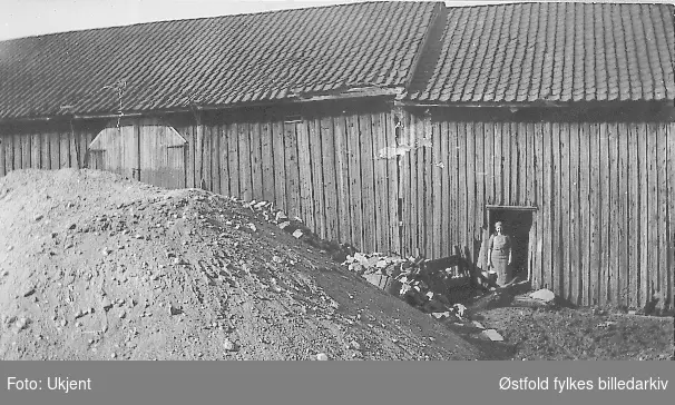 Den gamle lagården på gården Brunsby7/5  i Varteig ca. 1935.
Bygd i 1884 og revet i 1937. I døra står Johanne Brenne.
