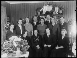 Gruppe med menn og kvinner i stueinteriør. 
På plate "Marie