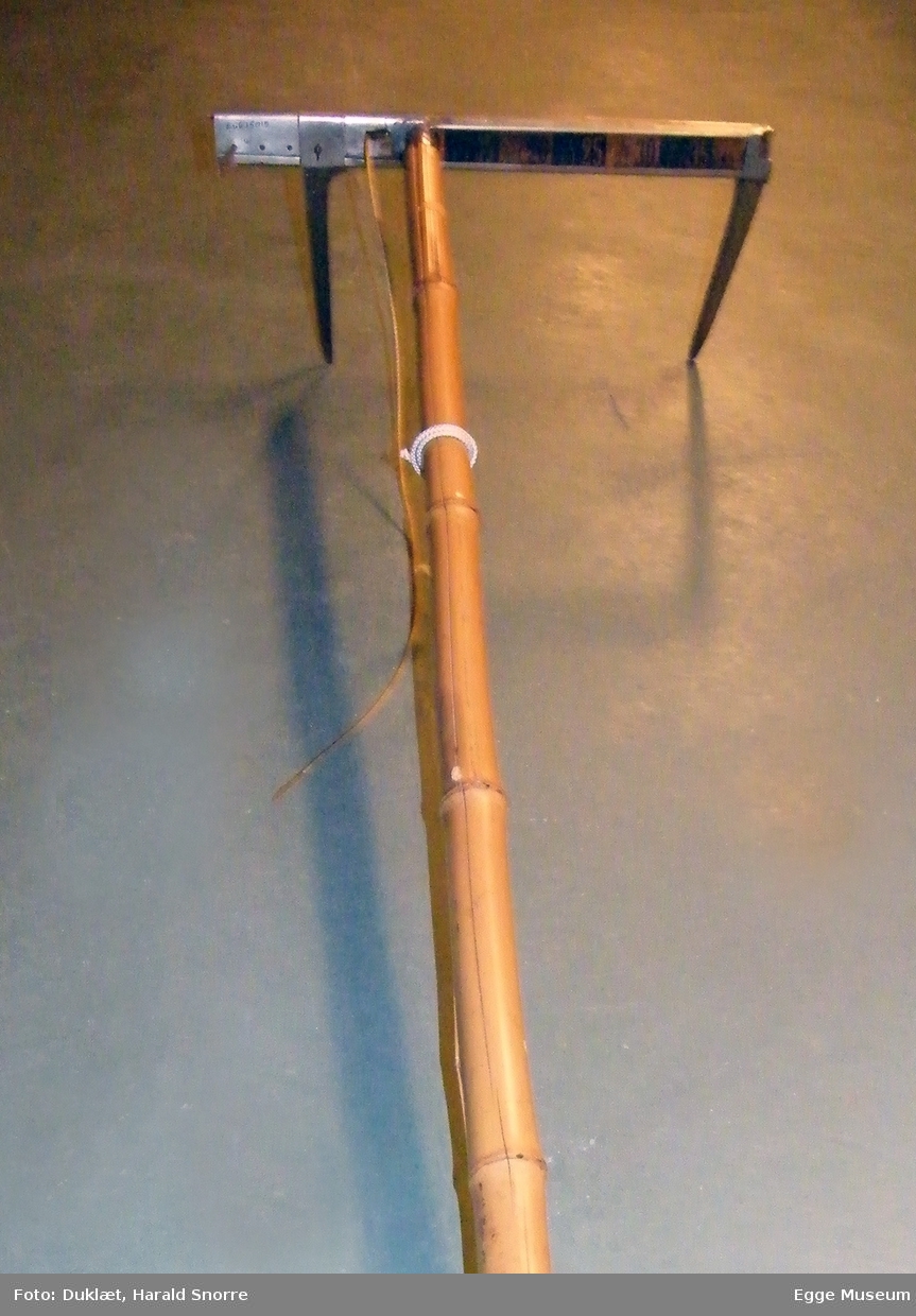 Klave for diametermåling. Klaven er laget i stål og har to armer, der den ene er bevegelig og kunne justeres med snortrekk. Armene er klinket fast til linjal. Papplate med måleenheter på linjal fra 0 til 40 i cm mål. Store tall som kunne leses på avstand. Bambusskaft, ant for kort.