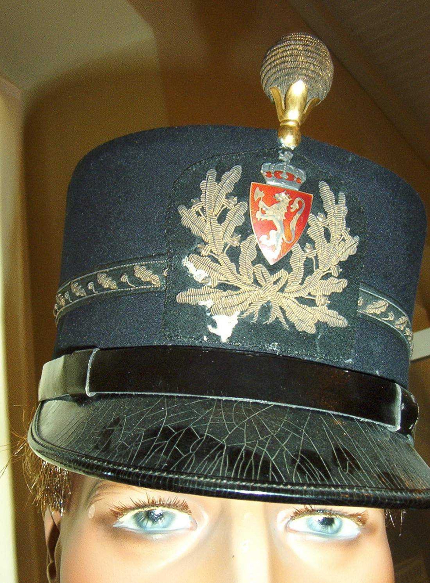 Uniformslue modell 1911. Brodert rundt Norske løve som er i emalje- rød og gull. Luemerket er litt skadet under metall broderi på høyre side av merket.