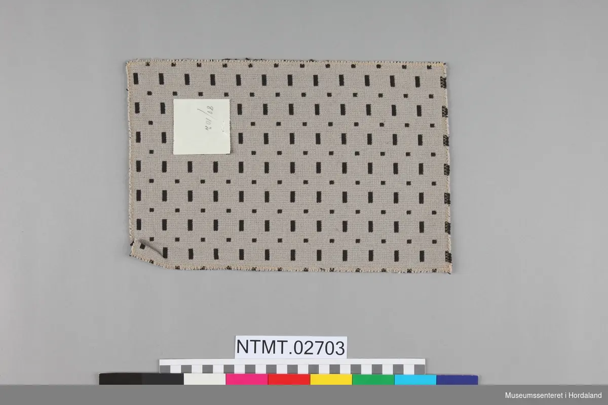 Innvevd mønster av små streker og firkanter i kontrastfarge, fordelt i stolper.