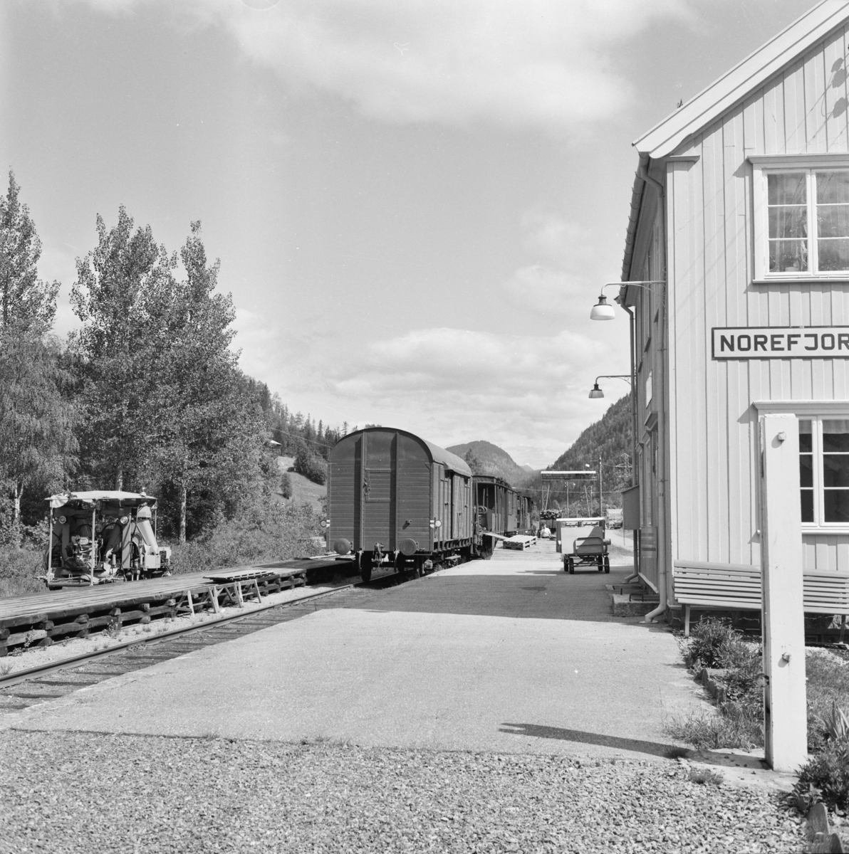 Godstog 5397 har stoppet på Norefjord stasjon for av- og pålessing av stykkgods. Til venstre en motorisert arbeidstralle for baneavdelingen.