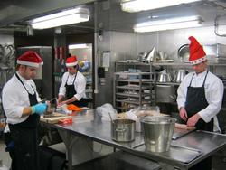 Tre kokker med nisselue tilbereder mat i kjøkkenet på en pla