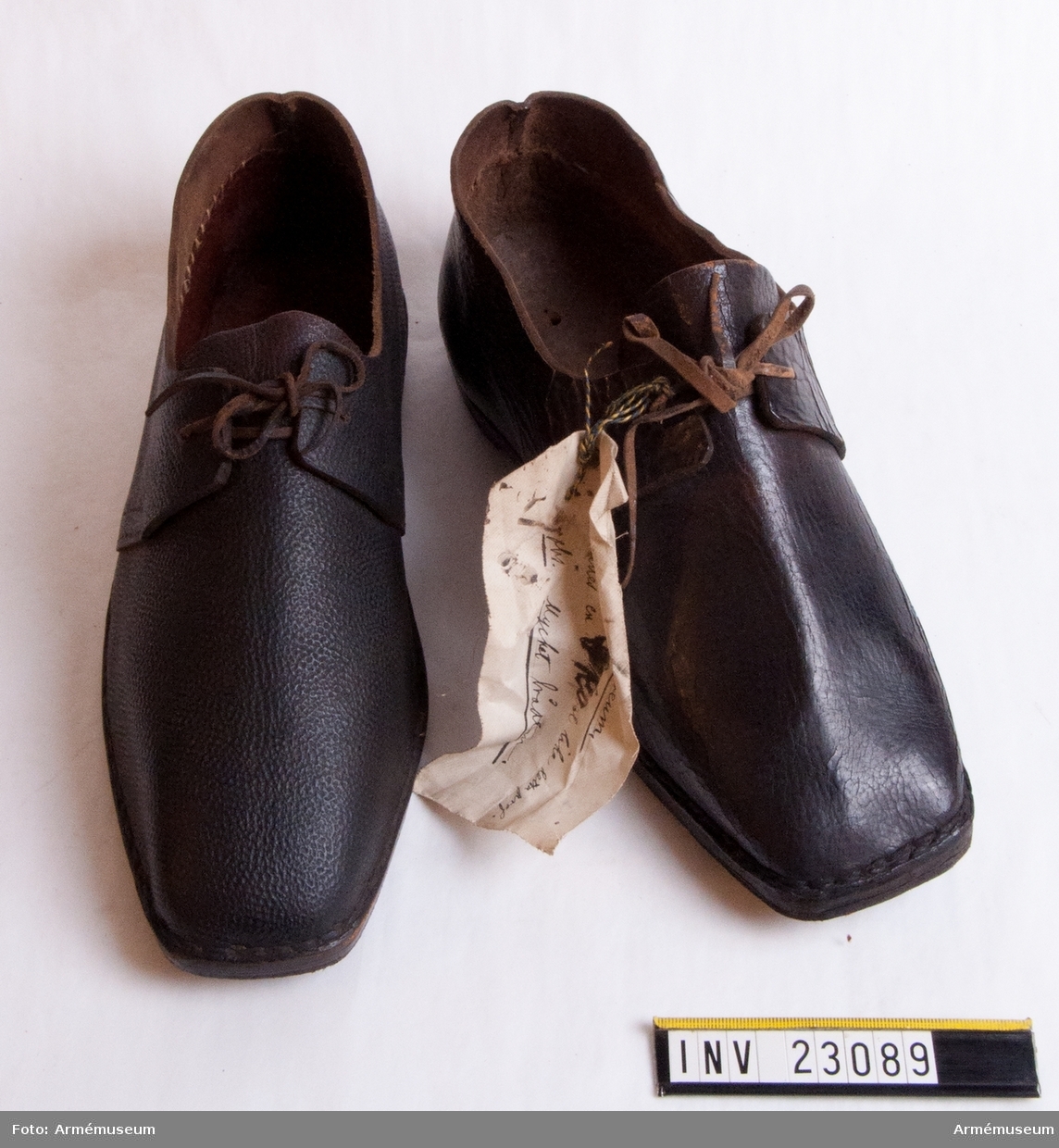Grupp C I.
Skor av brunt läder. En av skorna har rött lacksigill.

Vidhängande lapp på ena skon med text: "För Artillerimuseum, Beställer en sko lika detta prof. Obs. Mycket brådtom."