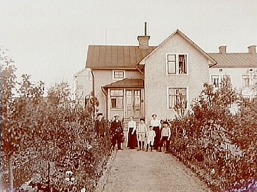 Näsbylund 2, Örebro öster.
Vinkelbyggt en och en halvplans bostadshus med glasad förstubro.
7 personer framför huset.
Karl Appelgren