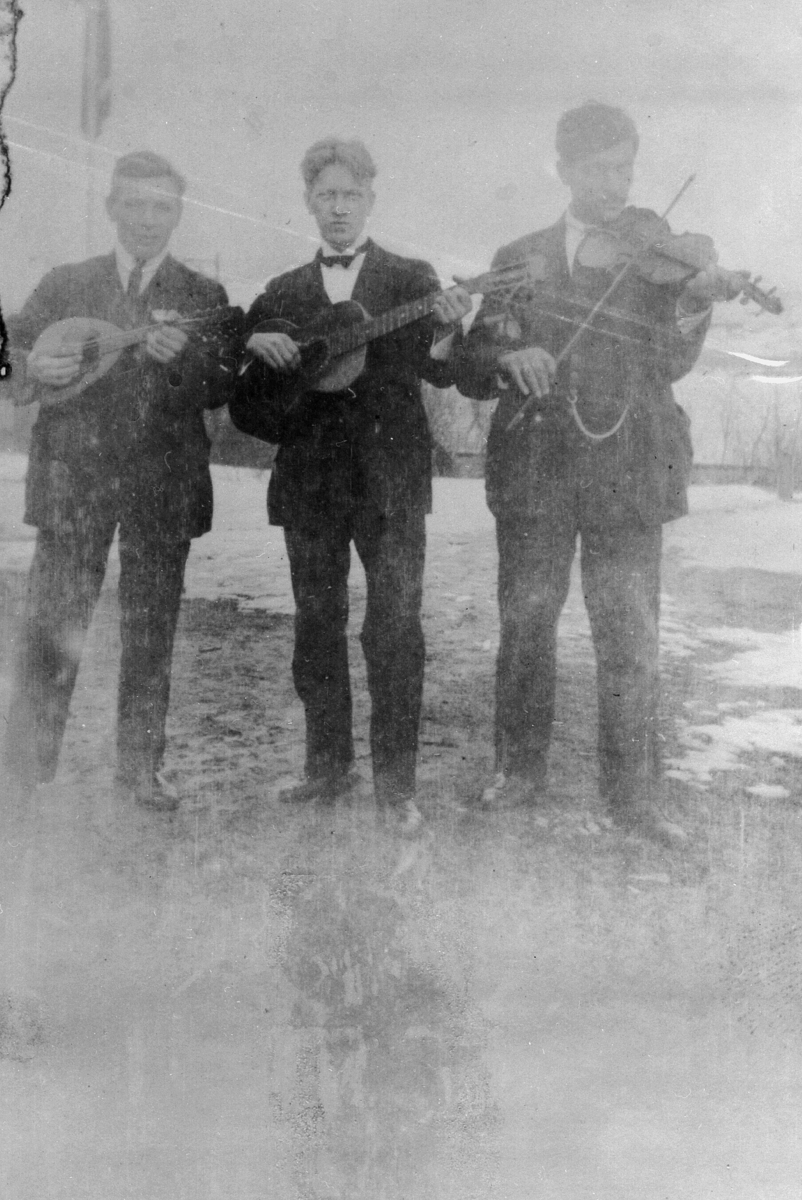 Tre menn med henholdsvis banjo, gitar og fiolin i dress. De er sansynligvis en gruppe som spiller til dans. Ingen årstall, men trolig fra før 2. verdenskrig.