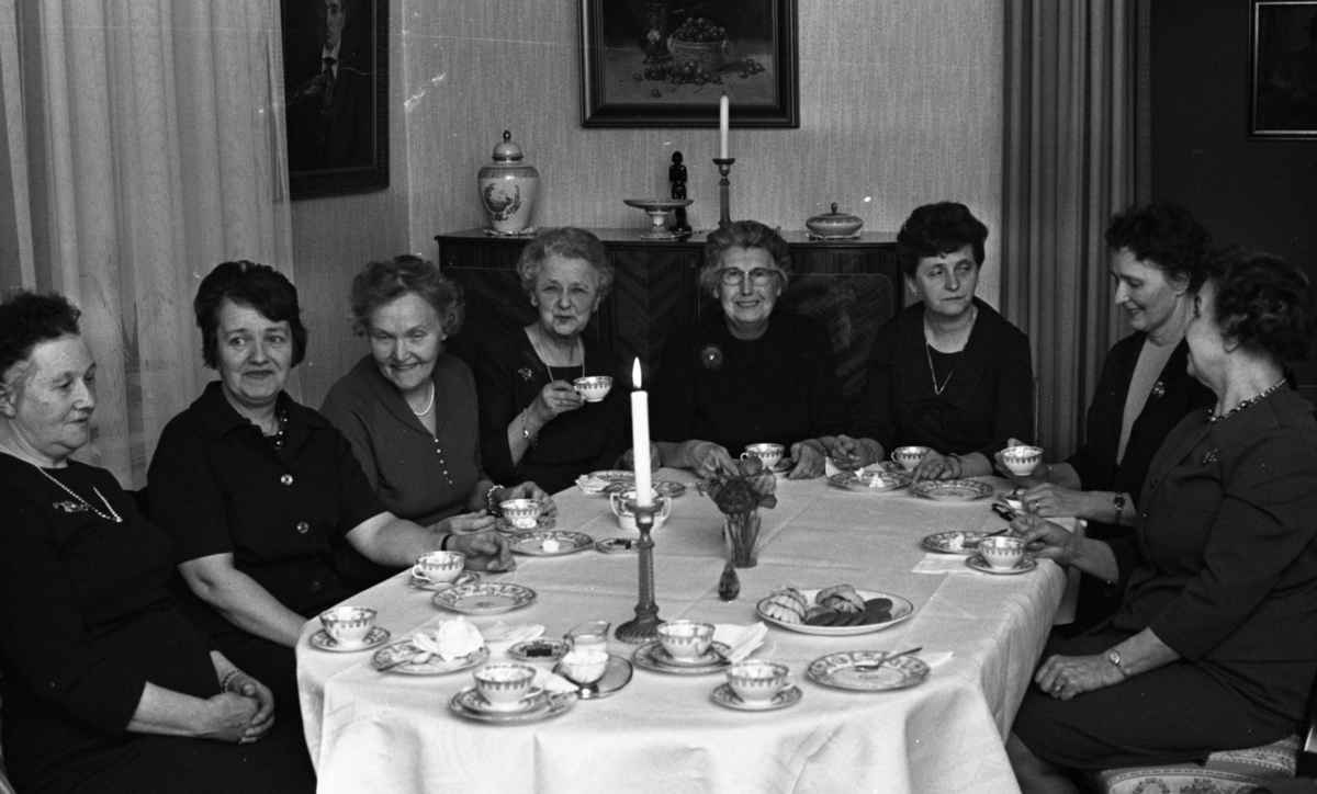 Syjunta, Biljard fritidssysselsättning 1 februari 1966

Åtta äldre damer sitter vid ett bord och dricker kaffe. På bordet ligger en vit duk och det är dukat med kaffekoppar, fat och assietter. En vas med blommor, ett tänt ljus i en ljusstake ett prydnadsföremål samt ett kakfat fyllt med kakor står står också på bordet. En byrå står i bakgrunden och tavlor hänger på väggarna.
