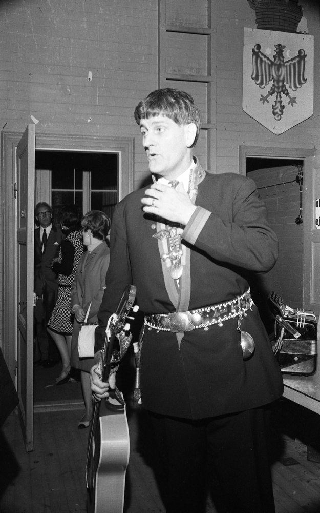 Natt 702, 12 juni 1967

Bild på Jokkmokks-Jokke när han är på väg in på en scen. Han bär samedräkt med samebälte runt livet samt bär en gitarr i handen. Andra personer syns i bakgrunden.