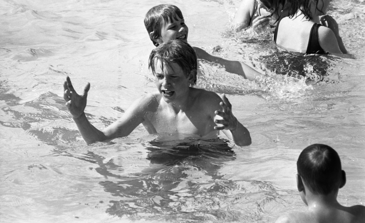 Gustavsvik 16 maj 1967Närbild på en pojke som badar tillsammans med andra ungdomar i utomhusbassängen på Gustavsviks badhus. Han har lyft båda sina armar.