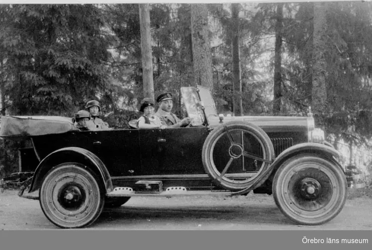 Två människor på åktur i en äldre bil. 
Bilen på bilden är en Maxwell från ca 1922-1925. Bilen hade registreringsnummer T2719 och registrerades den 27:e december 1924 på åkare Gunnar Blomqvist från Almby, Örebro. År 1930 fanns den kvar i bilregistret, numera ägd av byggnadssnickare Erik Eriksson från Östermalm, Lindesberg.