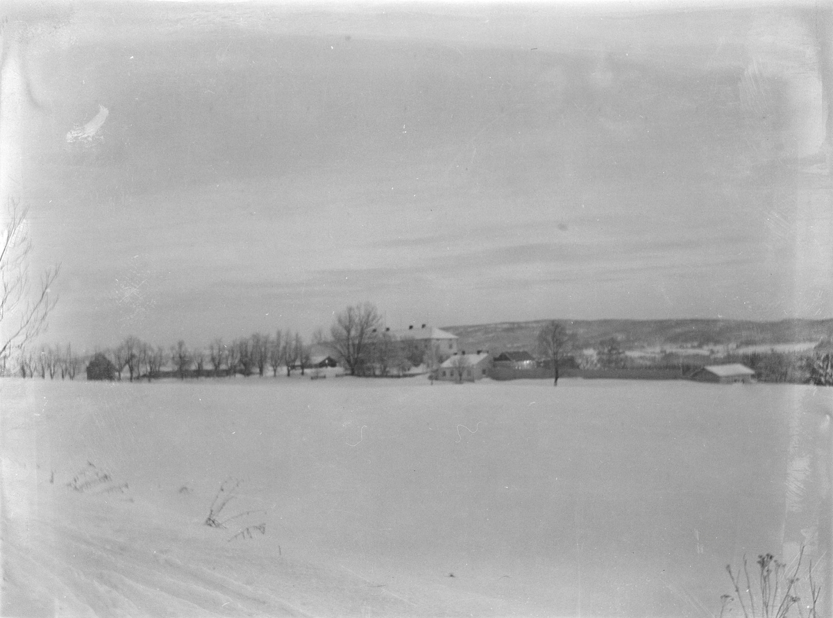 Linderud Gård med hele gårdsanlegget sett fra avstand med snødekte jorder i forgrunnen.