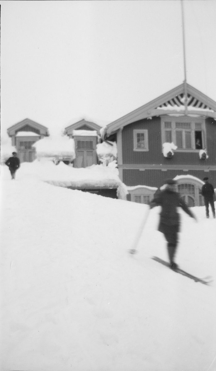 Mann uten ski og mann med ski er på vei ned fra taket på turisthotellet på Haugastøl stasjon via en bro av snø.