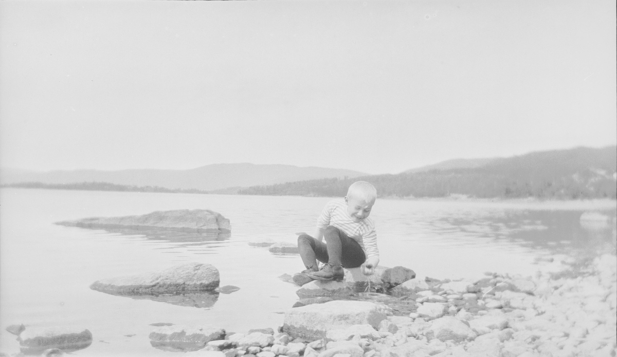 Iacob Ihlen Mathiesen sitter på huk i strandkanten. Han plukker opp noe fra vannet.