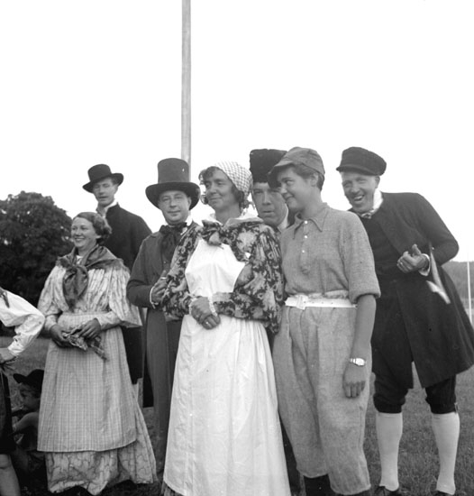 Festligheter vid Siggebohyttan den 30 juli 1937. De utklädda männen och kvinnorna deltar i någon form av dans eller teaterliknande folklustspel. Bakom dem syns en flaggstång.
