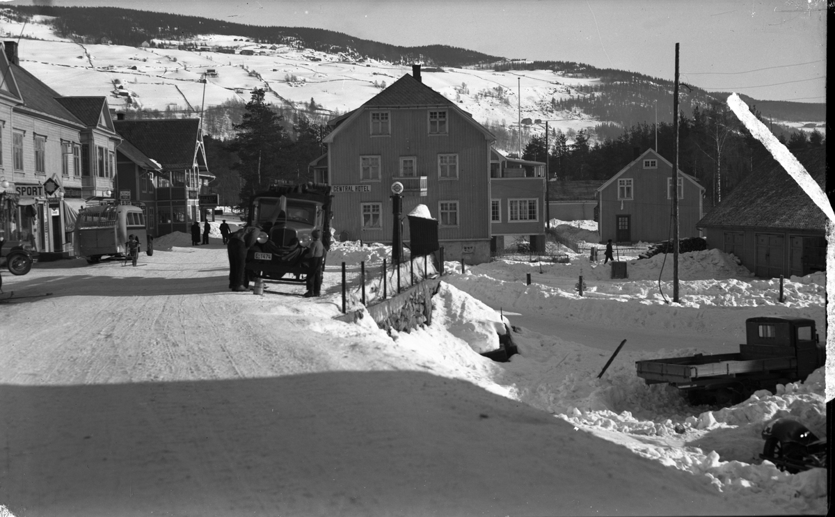 Biler og mennesker i snødekt gate på Fagernes, blant annet med Gullhagen-gården (til venstre), Elvely hotell og Central hotell.