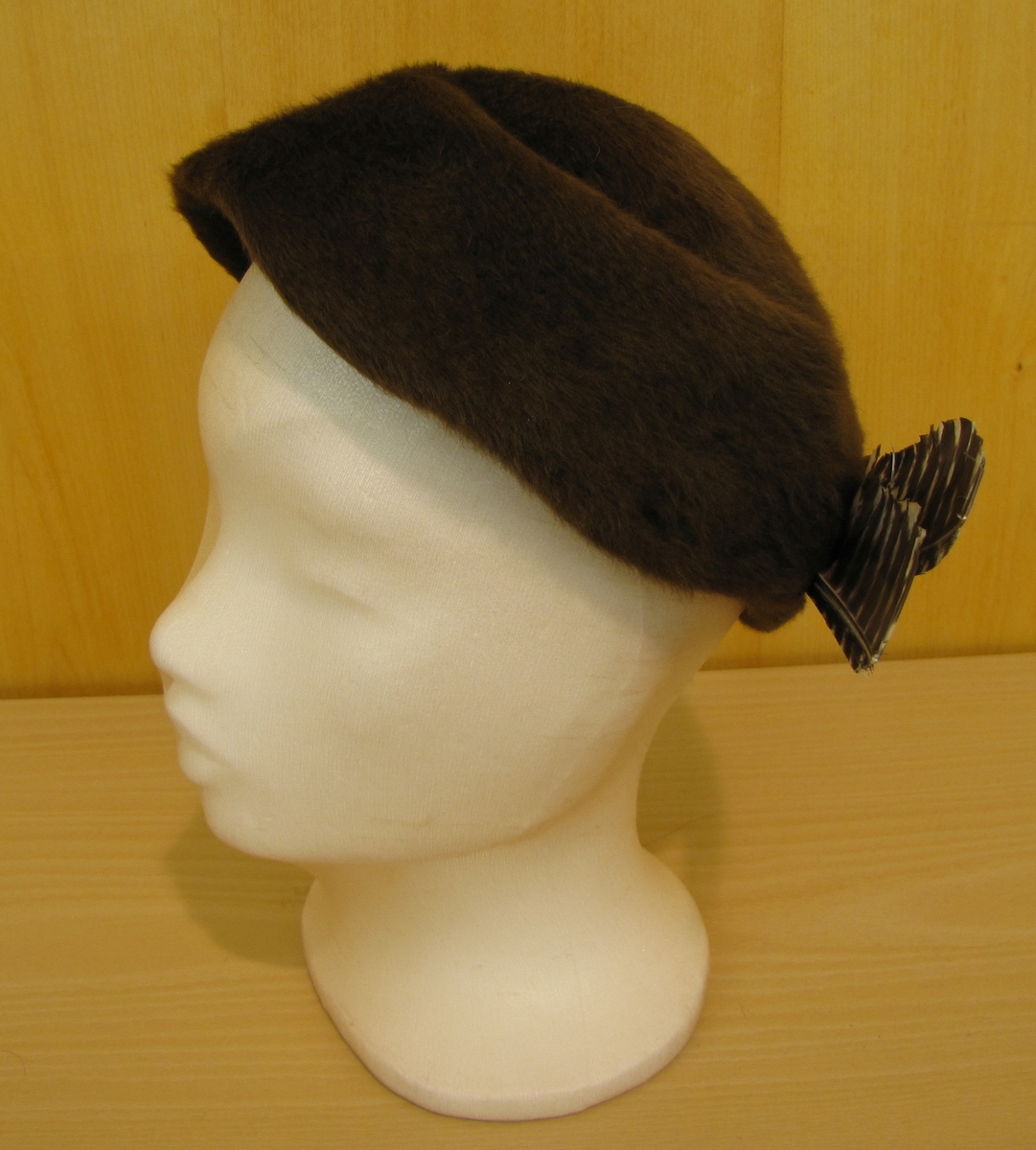 Rundkullig hatt utan brätte monterad med 2 bruna och vitspräckliga fjäderpennor.
Inköpt hos Strands eftr. Vänersborg.