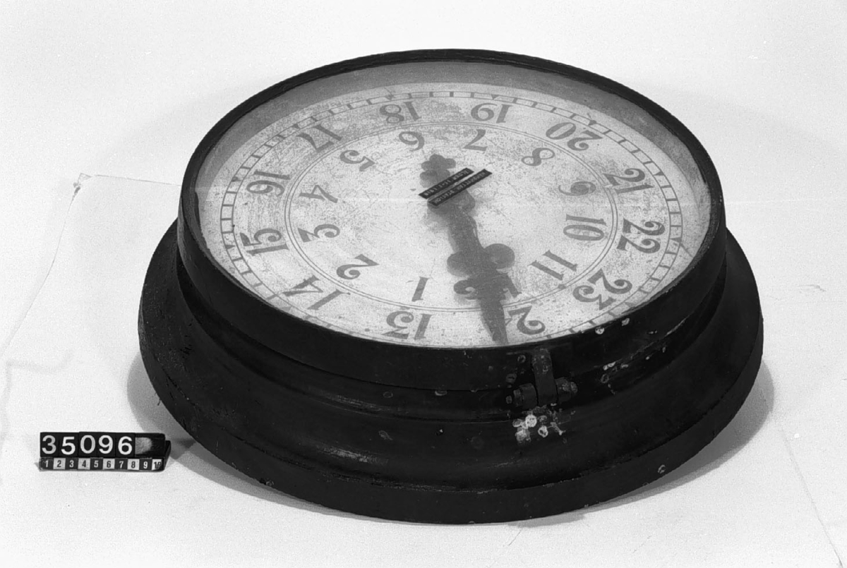 Pendelur i cylindriskt gjutjärnsfoder, med uppdragningsvev. Uret har loddrift med en veckas gångtid, 2 x 12 timmars urtavla, tim- och minutvisare.
