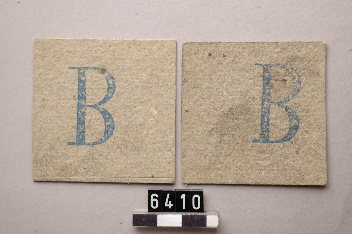Tre kolpolletter av papp, kvadratiska med bokstaven B. i blått tryck.