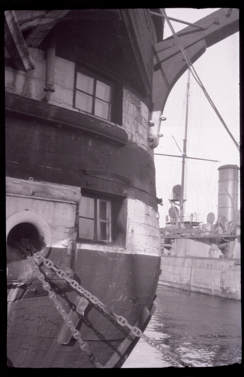 Bilden visar babords sida av linjeskeppets Stockholms bog. Fartyget är ombyggt till logementsfartyg, så att styckporter har blivit till fönster. Högst upp ser man vänstra kranbalken, i undre delen ankarkedjan. I bakgrunden ligger pansarskepp Dristigheten.