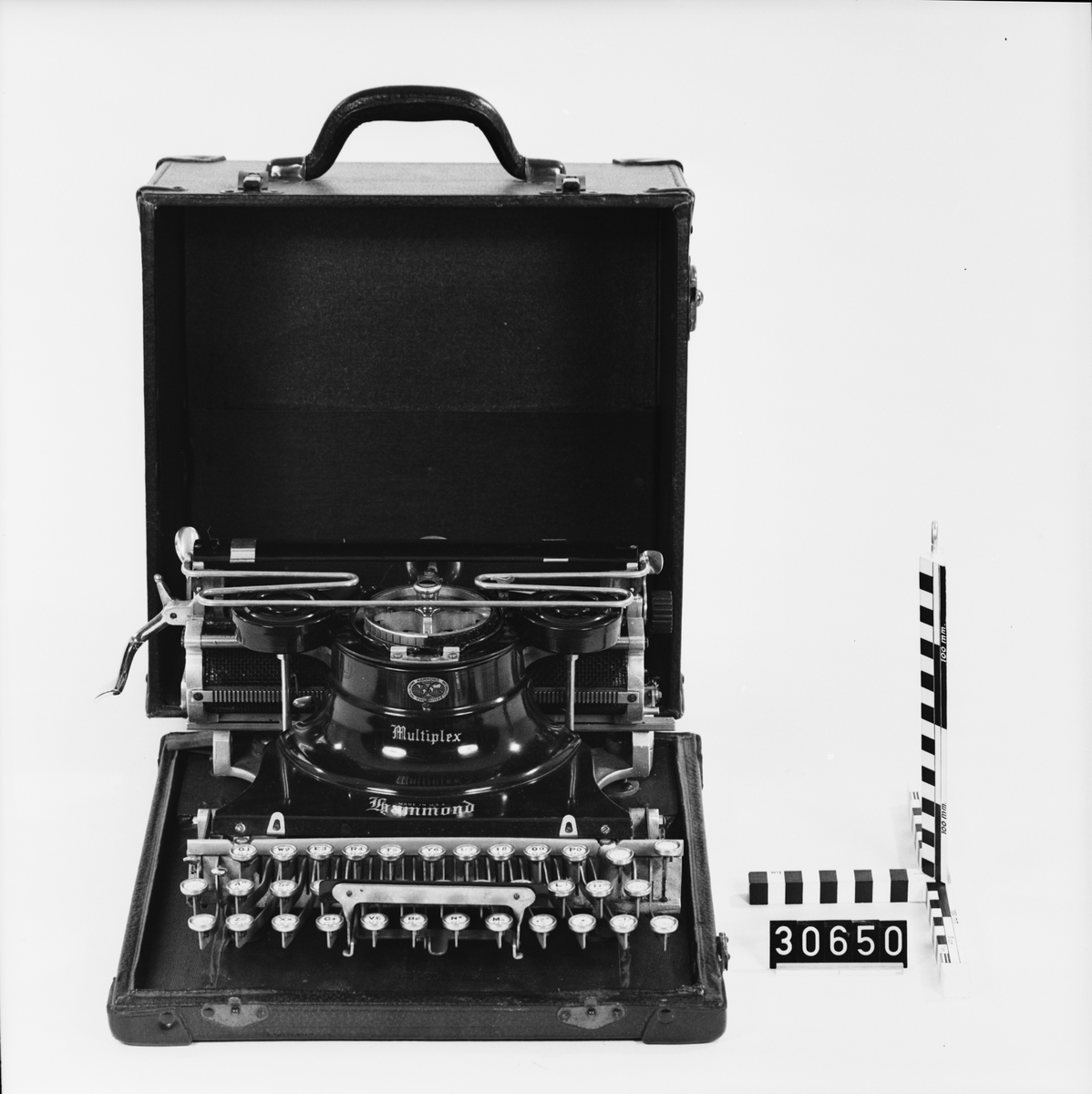 Svart skrivmaskin i en låda med hölje av pergamenterat trä. Maskinen är fastskruvad i lådan. Typer till mask, se TM 33.822-24.
Tillbehör: Låda.