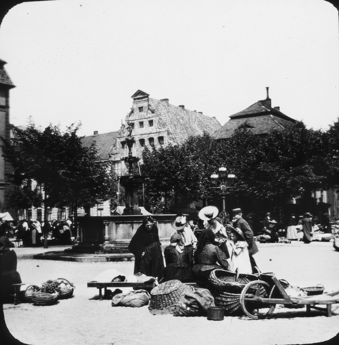 Skioptikonbild med motiv av kvinnor med korgar vid Luna-Brunnen på torget i Lüneburg.
Bilden har förvarats i kartong märkt: Resan 1906. Lüneburg 8.