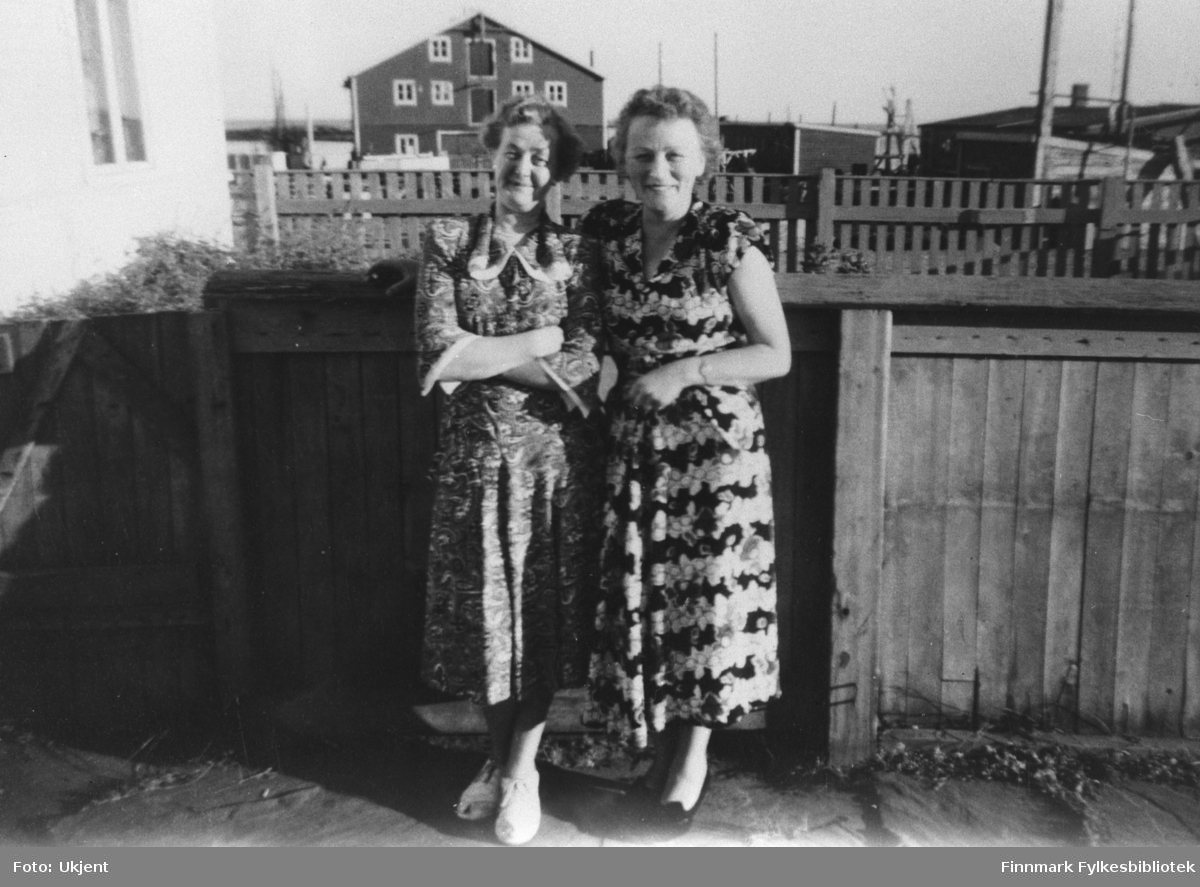 Bildet viser to kvinner. Damen til høyre er Klara Abrahamsen, gift med Thorleif Abrahamsen. Damen til venstre er Laila Aanstad, søster tli Thorleif og gift med Ivar Aanstad fra Vadsø. Bildet er tatt utenfor Abrahamsgården i Kiberg.