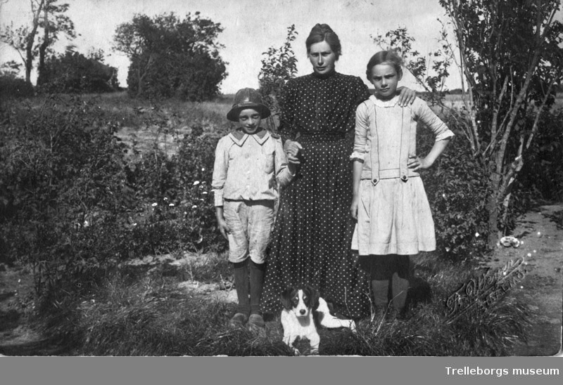 På bilden ser vi Berits farmor Anna född Persson 1884-08-11 maka till Magnus Jönsson och deras två barn Marta och Albert.Hunden heter Fylax.