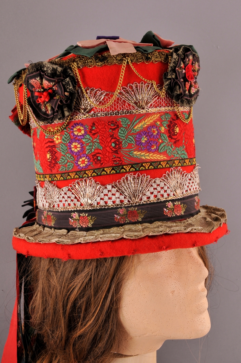 Brudehatt, nylaga. Oppbygd rundt ein filthatt av Zinkes mote AS. Langs bremmens ytterkant er det lagt ei "pølse" av vatt før heile hatten er kledd med høgraudt klede med tydleg lerretsvev. Inni går den raude kleden litt over halvvegs opp i hatten. Der er det  sydd ein løpegang med eit band til å dra saman vidda med, dette for at hatten skal slutte betre rundt hovudet. 
På bremmens overside er ei sylvbore foldelagt og sydd fast langs innerkanten, denne bora er truleg ikkje ny. Vidare rundt hattens pull er det sydd fast eit band med lansert blomemønster, ein sylvknipling, eit smalt band med brodsjert mønster og ein sylvblonde (ulik den som er lenger ned) og til slutt ei avklypt gullblonde/agraman heilt på toppen av pullens kant. Banda er i ein blandingskvalitet.
Over pullens topp (flat del) er ei sylvbore lagt i kryss, over denne er det festa rosettar sydd av grønt, lilla og rosa syntetisk band. Langs kanten av pullen er det sydd fast 3 rosettar, ein midt framme og ein på kvar side. I tillegg er eit "gull"-kjede av uedelt metall sydd fast så det heng i ujamne bogar.
Midt bak på hatten er det øverst sydd fast ei sløyfe av eit lansert bomullsband og ei mindre sløyfe nederst av eit mønstervove band. i tillegg ni lange heng av band, både einsfarga og mønstervove.