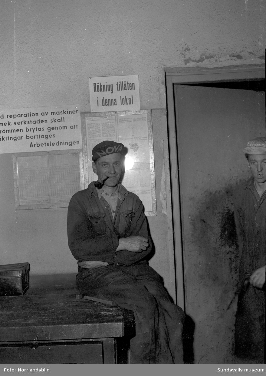 En piprökande man på Svartviksfabriken invid en skylt som upplyser om att rökning är tillåten på arbetsplatsen.
