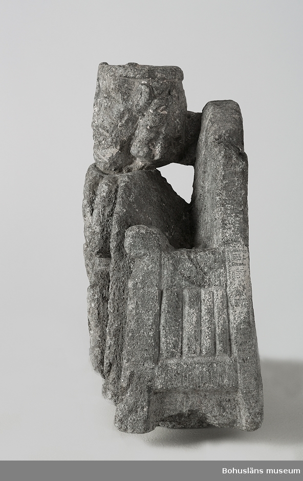 Stenskulptur av täljsten från Svarteborgs kyrka. Den helige Olof sittande i tronstol med högt ryggstöd. Han bär livbälte och mantel, en murkrona på huvudet, möjligen ett relikvarium i höger hand och håller vänster hand om skägget. Skulpturen är starkt eroderad.

Ur handskrivna katalogen 1957-1958: Olav d. helige, täljsten, Svarteborg. M: H. 41, största Br. 32,5 cm; krona och mantel, i höger hand spiran, vänster griper om skägget; sittande på en tronstol m. armstöd och högt ryggstöd, på alla håll smalnar stolen av uppåt. Starkt sliten.

Ur Katalog 1. Uddevalla Museihistoriska samlingar, svenska avdelningen. A. Yngre föremål. Upprättad av Knut Adrian Andersson 1916:                                                                                                                              No 34. Bild i täljsten av Olov den Helige. Yngre medeltiden, räknad till 1550. Förvarats i Svarteborgs kyrka under namnet "Kung Rane". Skänkt av församlingen år 1860-70-tal till Uddevalla museum. Förvaras ovanpå Medeltidsskåpet i sydvästra rummet.

Presenterad i  Uddevalla Museums tryckta katalog 1869 under rubriken 
F] Saker från yngre Medeltiden, räknad till 1550.
N:o 1. Bilder af S:t Olof i sten från Svarteborgs kyrka.

1861-1870 1 Arkeologiska och Etnografiska samlingarna U-a Museum D4A 1
Ur Gåvobok1864:
Svarteborgs församling:
Kristusbild af träd samt fragmenter af en Granit- [överstruket] Täljstensbild, enligt sägen föreställande Kung Rane, hvilka begge setat [överstruket] [oläsligt tillägg] i Svarteborgs kyrka. 
Tillagd kommentar av inrendent Knut Adrian Andersson; Olof d. Helige troligen.

Se foton på föremålet i Uddevalla museums kyrkliga utställning 1920, UMFA54467:0089.
Tillstånd, se Vårdblankett.