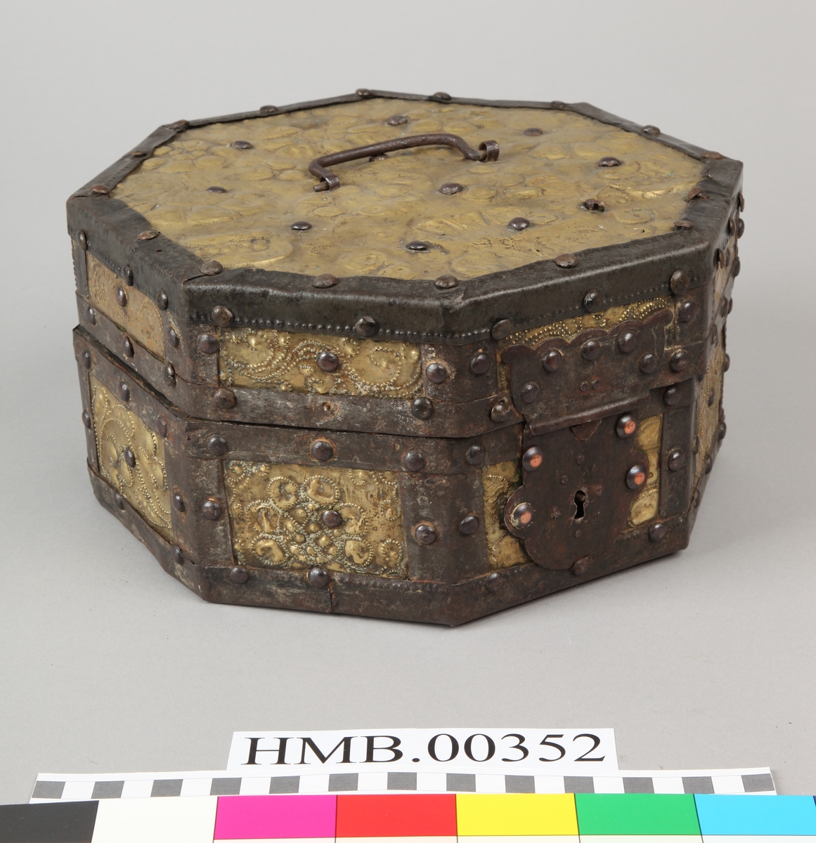 Åttekantet. Den har dekorerte flater i messing med jernbeslag og det hele er naglet på tre. På lokket er det en hank. Flaskefôret er låsbart, men den originale nøkkel mangler.