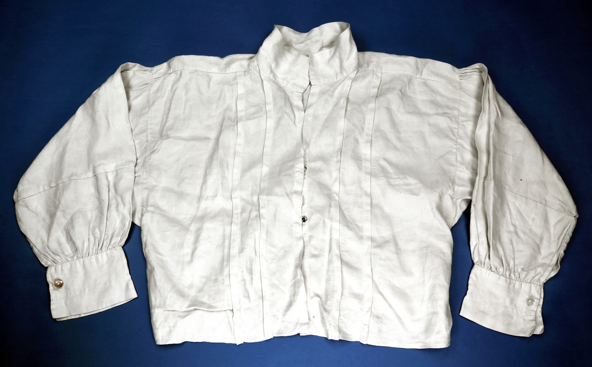 Skjorte av lin med folder/ legg i framkant, vide ermer som er rynket mot mansjett og fra skuldrene, og med trykknapper i front