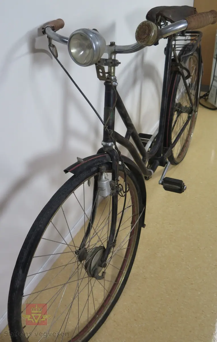 Tråsykkel, damemodell. Har to hjul, styre, sete, pedaler, frontlykt, ringeklokke, bagasjebrett, dynamo og refleks bak. Svart med rød staffering. Brunt sete og røde holker på styret. Sykkelen er i hovedsak lagd av metall, gummi og skinn.
Emblem med teksten: REIDAR KVAM Ø. GAUSDAL MIL.