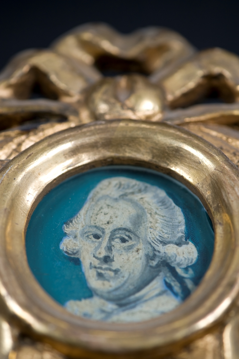 Tvådelad ram med spegel och en akvarell. Målningen bär texten "Amphion Cap:t Jonas Pettersson, Ancona 1795." Över spegeln sitter även ett litet runt mansporträtt i akvarell. Den förgyllda ramen är krönt med bladornament och en rosett med hängande ändar.