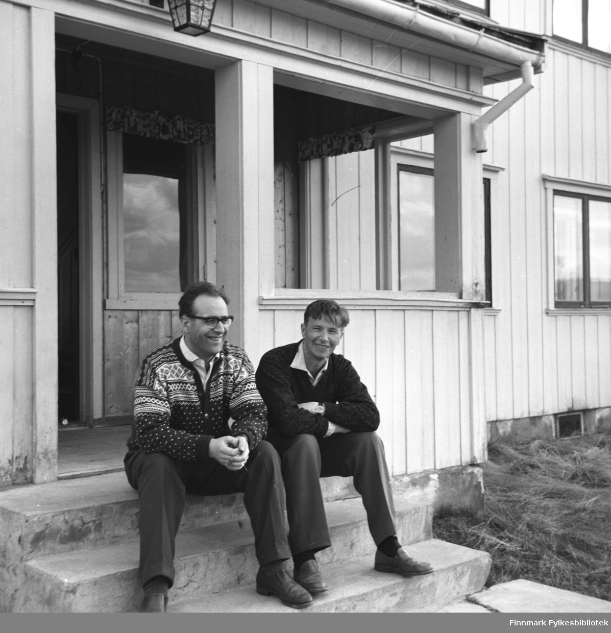 To menn sitter på trappa til en bygning i Karasjok. Mannen til venstre på bildet er ukjent og ved siden av han sitter Eino Drannem.