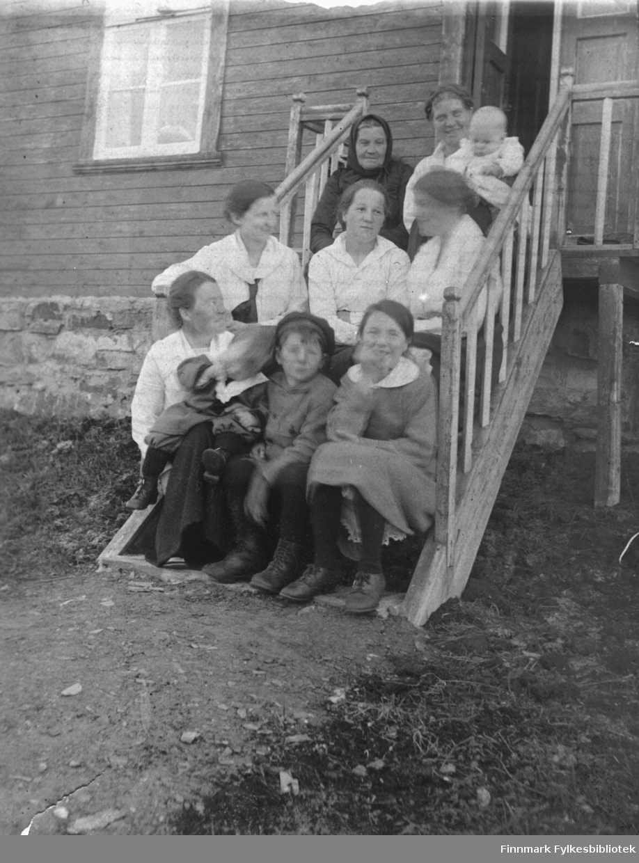 Gruppebilde av kvinner og barn sittende i ei trapp i Kjelsvik, ca. 1900? Påskrift bak på bildet: 'Fra Kjelsvik. Gustavs hus. Bestemor Fikse' - sistnevnte het Maren Dorthea Jakobsdatter Fikse, og sitter øverst til høyre. B 5729