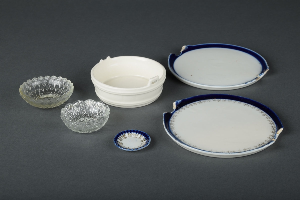 Diverse servisedeler til dukkelek - to glasskåler, en liten asjett, en hvit skål og to tallerkener av keramikk.