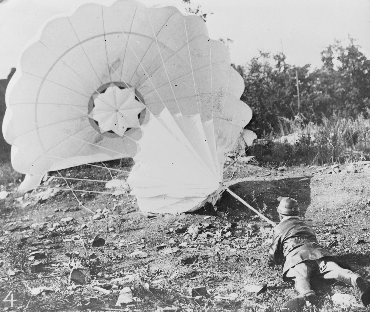 Fallskärmsprov på Malmen, omkring år 1920. En man har landat på marken med en fallskärm framför sig på Centrala Flygverkstäderna i Malmslätt.
