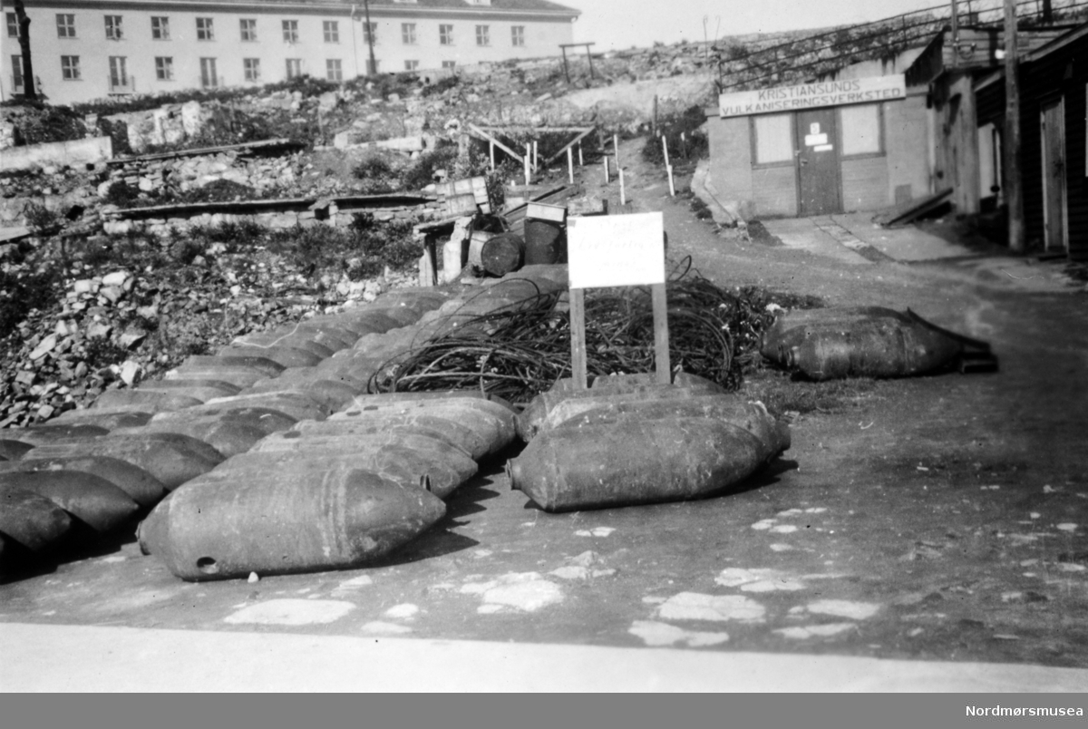 Tyske flybomber ved Kristiansund Vulkaniseringsverksted. Tyske stridsvognsminer og personellminer hadde en helt annen utforming enn de flybombene som er avbildet. Det står "miner" på advarsels-plakaten. Dette skiltet kan ha henvist til at tyskerne også minela området eller at de brukte mineskiltet som en generell advarsel. (Info: Johan B. Siira).  Miner var installert under Storkaia for å sprenge denne i luften ved en eventuell alliert invasjon av byen. Etter kapitulasjonen 8. mai 1945, ble disse minene tatt opp av tyskerne. I bakgrunnen ser vi nye Grand Hotell. Bildet er datert 20. mai 1945. Det står "miner" på advarsels-plakaten.  Fra Nordmøre Museums fotosamlinger.