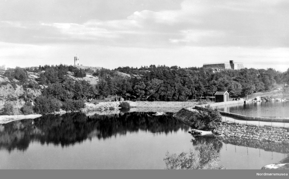 Vanndamman i byparken, her med 2 av de totalt 4 dammer, som totalt utgjør Vanndamman på Kirkelandet. Oppbyggingen av et regulært vannverk for Kristiansund skjedde da brann- og veiinspektør Peder Rosentræder i slutten av 1850- årene planla og oppførte en dam som lå like ovenfor Roligheten, og som senere fikk navnet Svanedammen på folkemunne, og som nå er den minste av de 4 dammene. I bakgrunnen litt til venstre, ser vi Varden i det fjerne. Fra Nordmøre Museum sin fotosamling. Serie