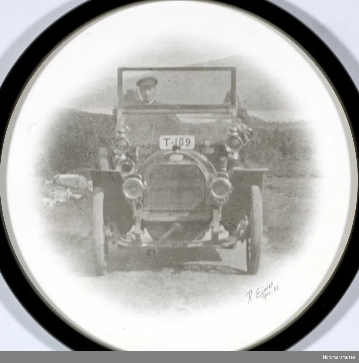 bil, med registreringsskiltene T-109 plassert på toppen av radiatoren. Datering av fotografiet er usikkert, men trolig omkring 1903 til 1910. Bildet er reprodusert i 1982 av R. Eidem. Se også reg. nr. KMb-2008-050.0051. Fra Nordmøre museums fotosamlinger.





Bilen er ikke en Ford T, bl.a. fordi den hadde forfjær på tvers over forakselen. Denne har langsgående fjærer. Skiltet er ikke plassert på toppen av radiatoren (upraktisk), men i  nerkant av frontruteramma. Registreringsnummeret T-109 viser at bildet ikke kan være tatt før 1. april 1913. Først da trådte motorvognloven av 1912 i kraft, som innførte fylkesbokstav på bilskilt.
Ivar E. Stav - 27.09.2016 kl. 14:10

Stoewer 1911. Se kommenterer på annet identisk bilde.
Trygve Krogsæter - 27.09.2016