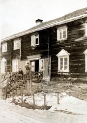 Foto av tre mennesker utenfor et eldre tømmerlån. Bildet er 