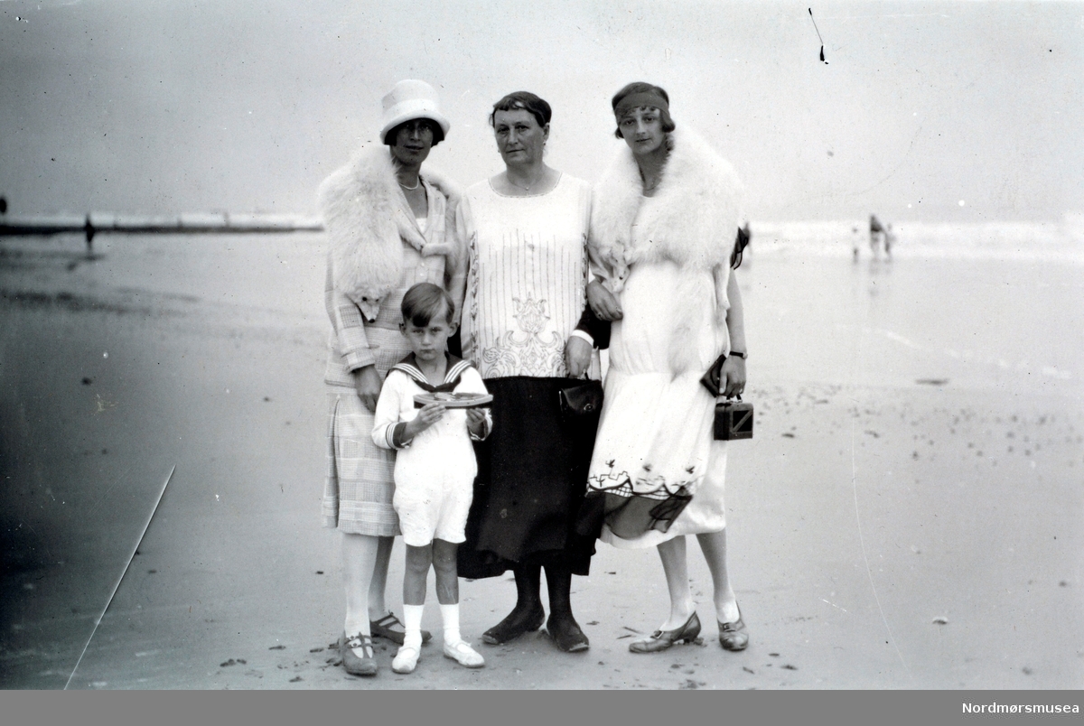 Foto av en gruppe kvinner og en gutt på stranden, ukjent hvor. Kan være i Tyskland eller England, men også andre land er mulige. Datering er usikker, menkan være fra tiden rundt 1920 til 1927. Fra Ida M. Knudtzons fotosamlinger, nå en del av Nordmøre Museums fotosamlinger.