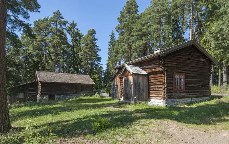 Husmannsplass med brunlig hus i halvannen etasje og med tilbygd vindfang, og en gråbgun tømmerlåve med utedo ved siden av.