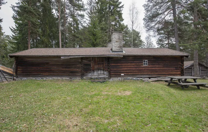 Langt størhus i brunlig tømmer, med stor plen og et parkbord utenfor.