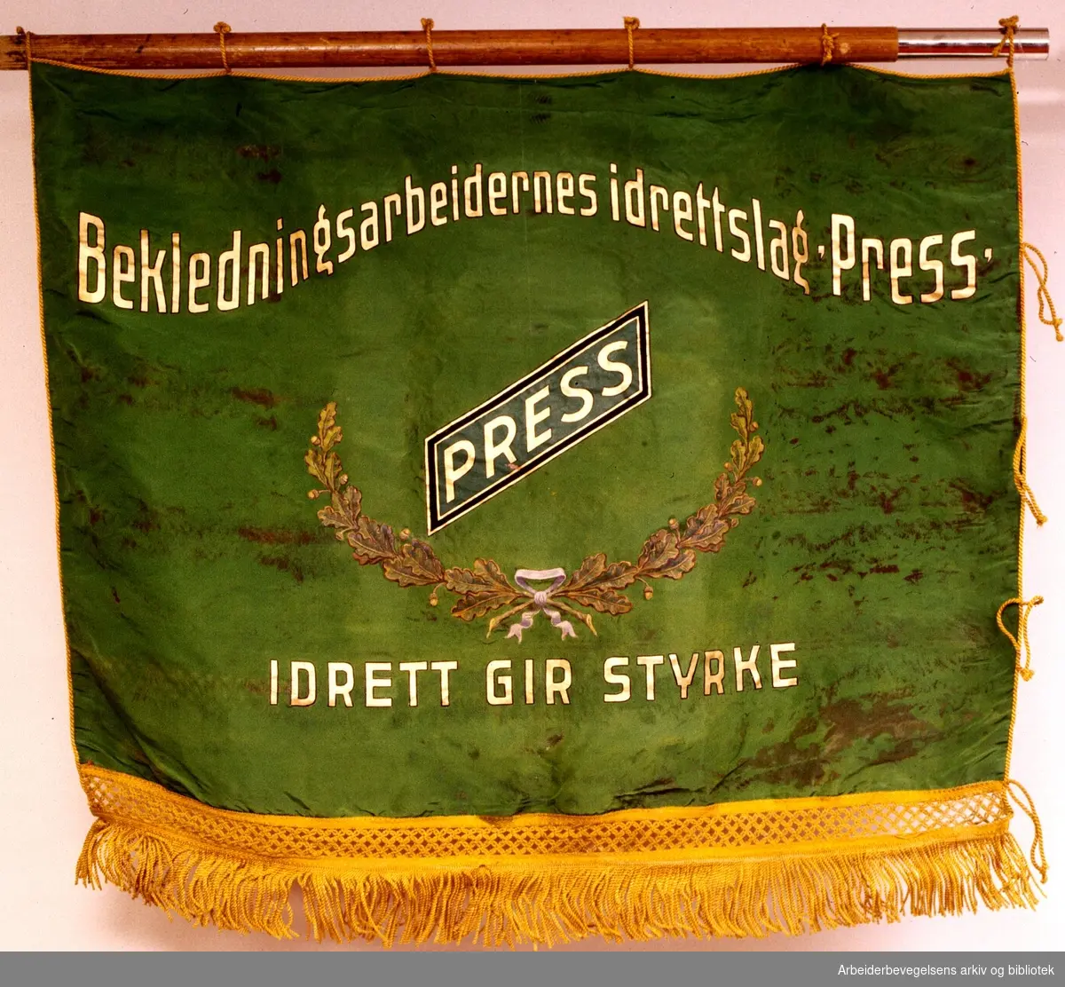 Bekledningsarbeidernes idrettslag Press.Stiftet 25. mai 1932..Bakside..Fanetekst: Bekledningsarbeidernes idrettslag "PRESS". Idrett gir styrke...